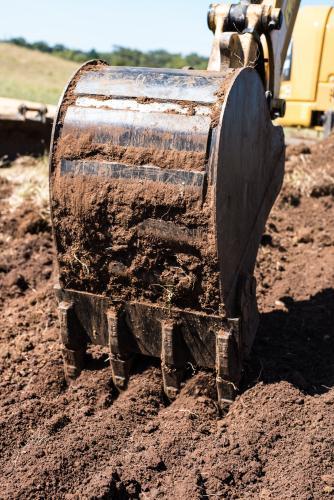 Toothed excavator bucket digging in brown soil - Australian Stock Image