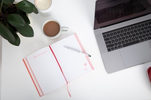 top down desk view of laptop, mug of hot chocolate and journal - Australian Stock Image