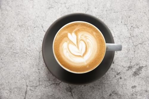 Top-down shot of flat white in mug on black saucer - Australian Stock Image