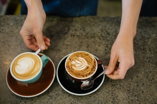 Top shot of a barista's hands serving artistic coffees - Australian Stock Image