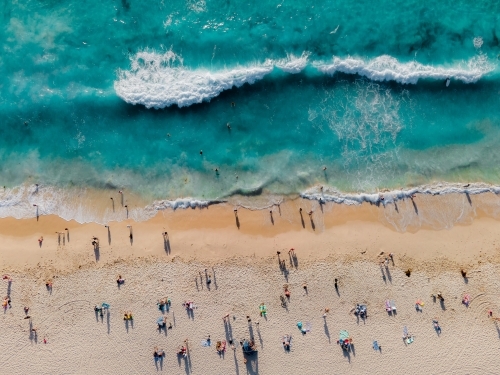 top shot of a beach with waves. people swimming and sitting on white sand shoreline. on a sunny day - Australian Stock Image