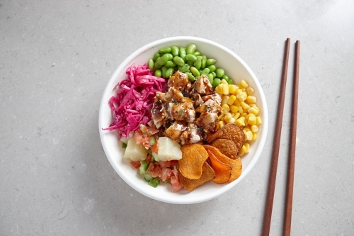 top shot of a bowl of chicken vegetable salad with wooden chopsticks on top of a grey background - Australian Stock Image