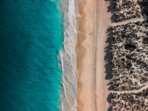 top shot of a waves in a shoreline with white sand, grass and ocean water - Australian Stock Image