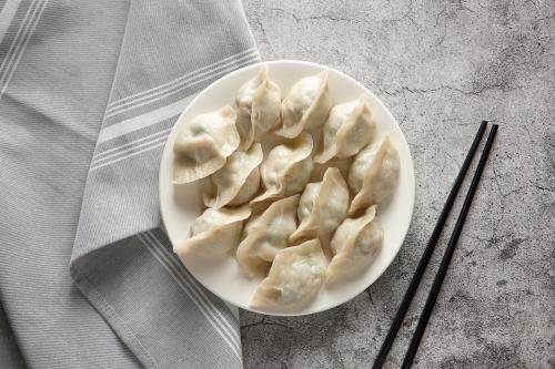 Steamed dumplings on a plate with chopsticks on the side - Australian Stock Image