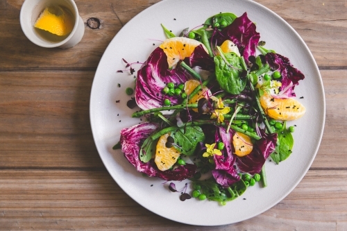 Top view of a mandarin, radicchio, pea and baby spinach salad on timber table - Australian Stock Image