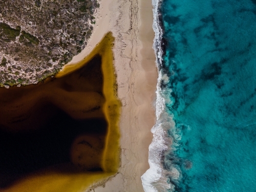 top view shot of a beach with white and yellow sand, bushes, and waves on a sunny day - Australian Stock Image