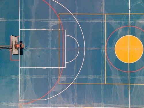 top view shot of a dark blue half basketball court with colorful lines and yellow circle - Australian Stock Image