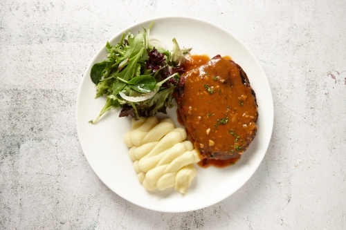 top view shot of a steak with mashed potato and salad on the sides all placed on a white plate - Australian Stock Image