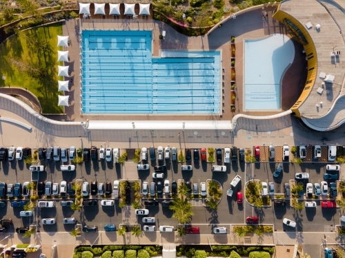 top view shot of two swimming pools with white shade in the sides, trees and cars in a parking lot - Australian Stock Image