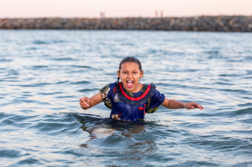 Torres Strait Islander child swimming in ocean water at dusk shouting loud - Australian Stock Image