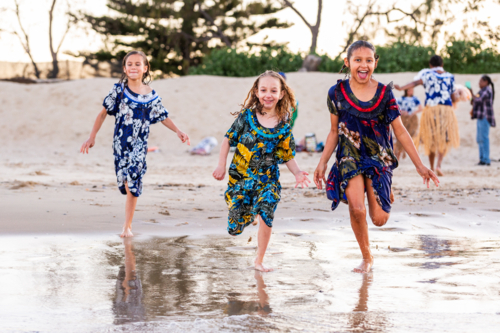 Torres Strait Islander children running and splashing into ocean water at dusk on Australian coast - Australian Stock Image