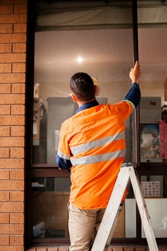 Tradie standing on ladder replacing screen of window - Australian Stock Image