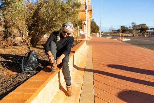 traveller sitting on wall adjusting hiking boot - Australian Stock Image