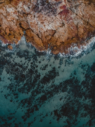 Turquoise blue water crashing against orange rocky shore – abstract aerial - Australian Stock Image