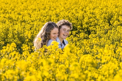 Tween boy and teenage girl cuddling in laughing in canola field on farm - Australian Stock Image