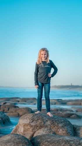 Tween girl standing on rock at the beach - Australian Stock Image