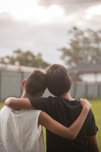 Two aboriginal boys with their arms around one another looking away - Australian Stock Image