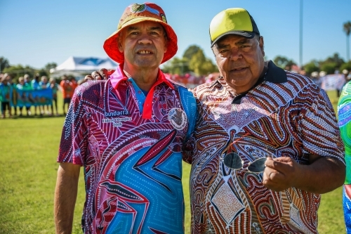 Two aboriginal males in hats standing with arm around each other