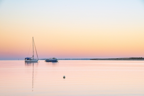 Two boats sailing on calm water at dawn in the bay. - Australian Stock Image