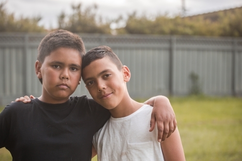 Two boys with their arms around each other while standing outdoors - Australian Stock Image