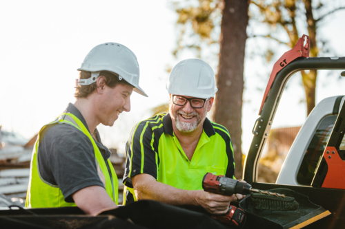 Two builders standing next to ute on construction site one man holding a drill - Australian Stock Image