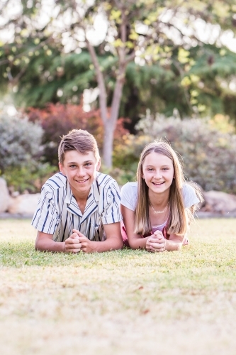 Two children brother and sister lying on grass happy - Australian Stock Image