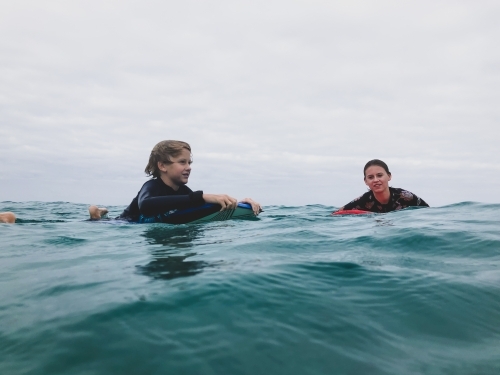 Two children floating on boards in ocean on overcast day - Australian Stock Image