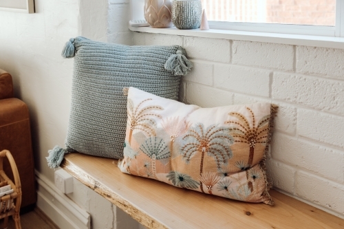 Two decorative pillows on a wooden bench against the brick wall. - Australian Stock Image