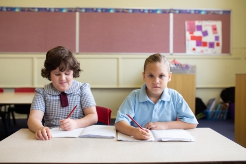 Two girl students writing in a primary school classroom - Australian Stock Image