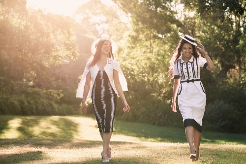 Two girls in dresses walking in the park backlit by sun - Australian Stock Image