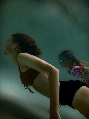 Two girls swimming underwater in a pool, side view - Australian Stock Image