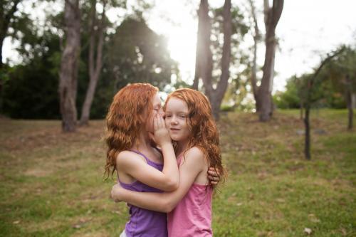 Two girls telling secrets in a field