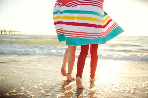 Two girls walking on the beach sharing a beach towel - Australian Stock Image