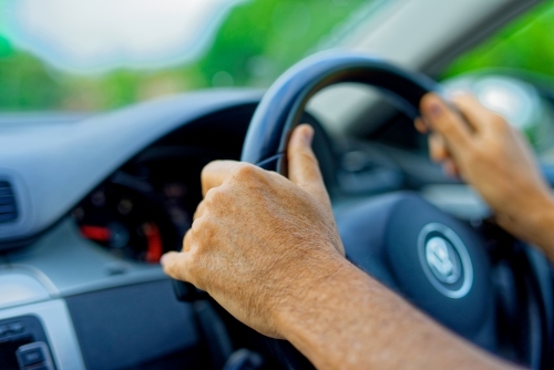 Two hands on steering wheel driving a car on suburban roads - Australian Stock Image