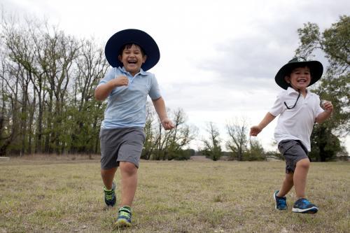 Two laughing boys wearing school uniform running across grass - Australian Stock Image