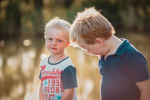 Two little boys exploring near river on an afternoon adventure in the Australian bush - Australian Stock Image