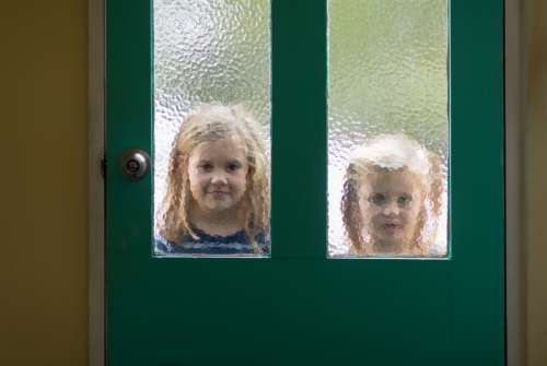 Two little girls outside looking in through door - Australian Stock Image