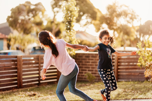 Two little girls playing holding hands in the front yard - Australian Stock Image