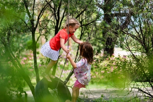 Two little girls playing on a tyre swing on a gum tree in the front yard of a rural property - Australian Stock Image