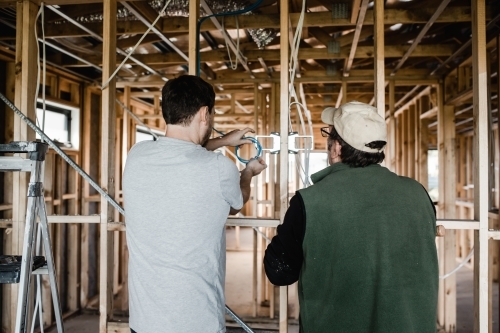 two men are laying cables in a house at frame stage - Australian Stock Image