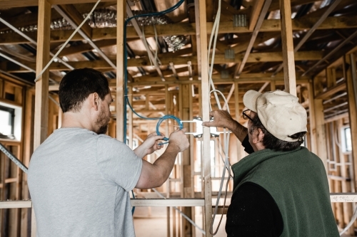 two men are laying cables in a house at frame stage - Australian Stock Image