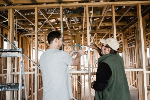 two men are laying cables in a house at frame stage - Australian Stock Image