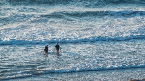 Two surfers with boards entering the surf - Australian Stock Image