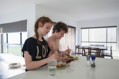 Two teenage children eating breakfast at home