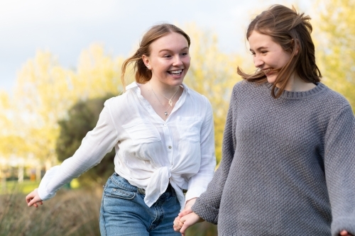 two teenage girls holding hands in natural setting - Australian Stock Image