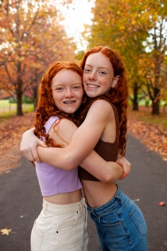 Two teenage girls standing in a street lined with Autumn trees - Australian Stock Image