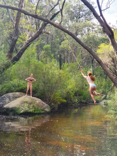 Two teenage girls swinging on a rope swing at a rock pool - Australian Stock Image