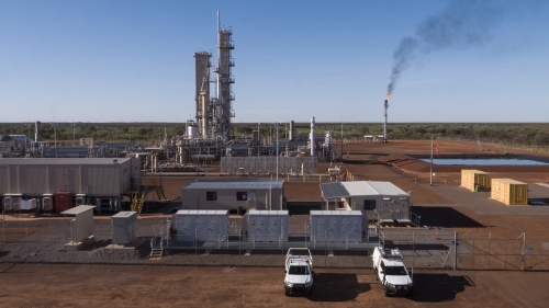 Two white work cars parked outside a power plant with a smoking flue-gas stack - Australian Stock Image