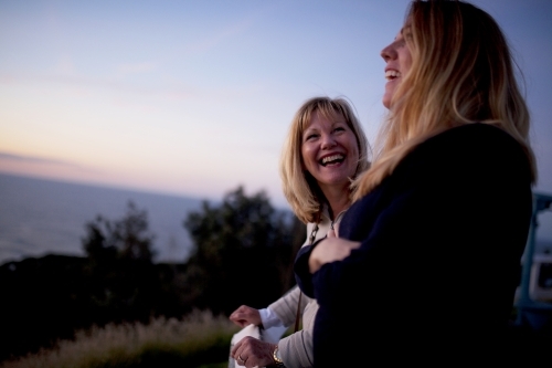 Two women standing at a lookout at dusk, laughing - Australian Stock Image