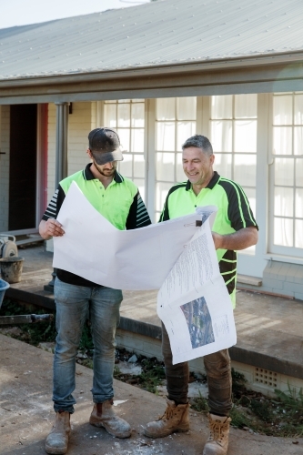 Two workers discussing building plans at a construction site - Australian Stock Image